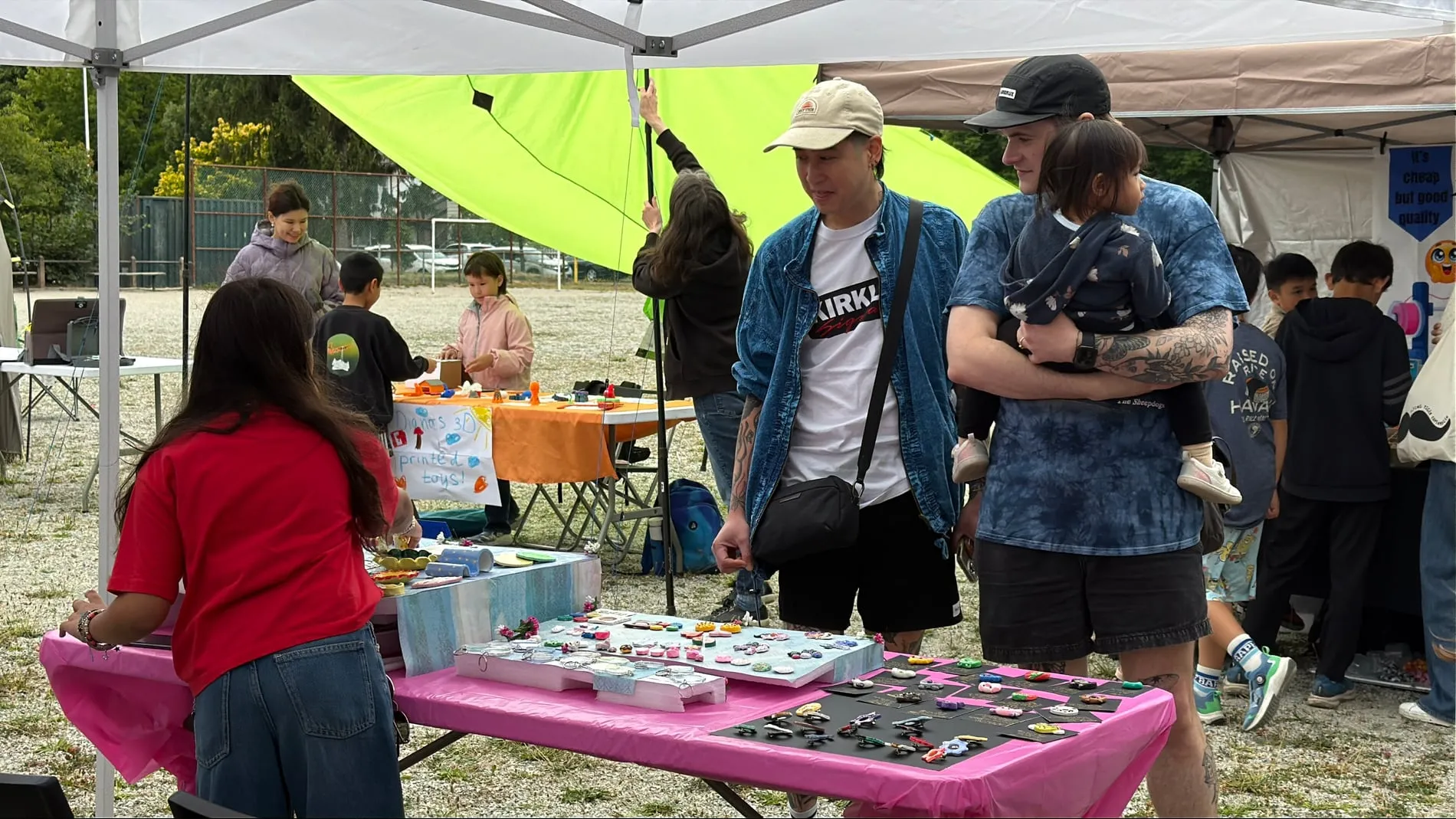 Visitors browsing booths on the gravel field, past tables of small handmade goods and hand-lettered signs.